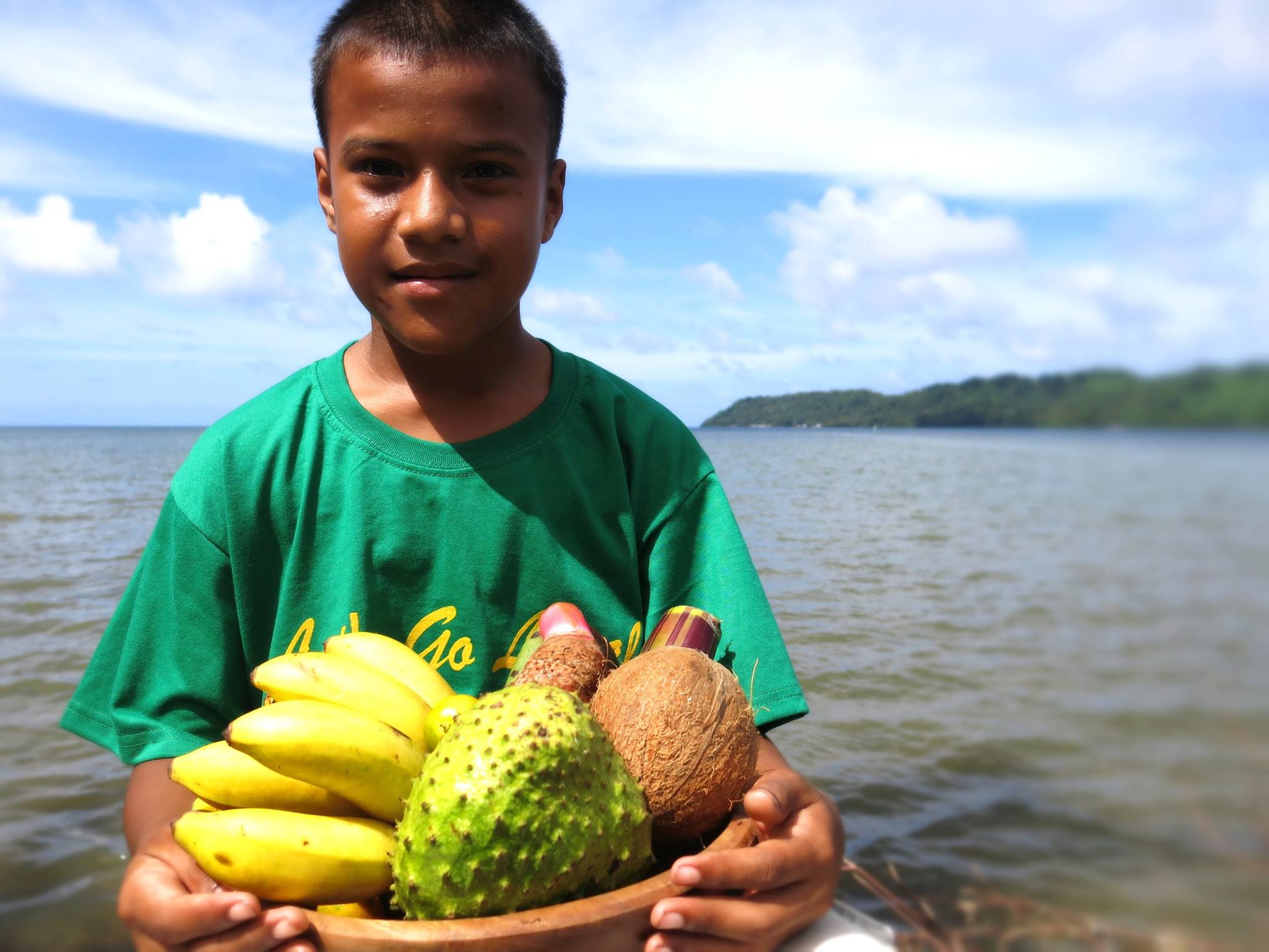 Young boy from Federated States of Micronesia (FSM) poses for a photo holding a bowl of fresh fruit.