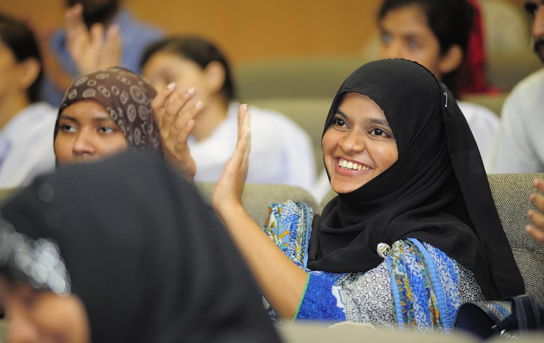 Young person in Pakistan smiling and applauding at an event