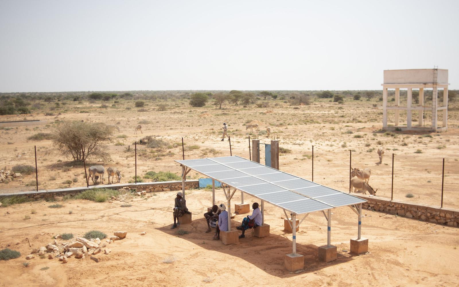 Local residents sit under an array of solar panels used to help pump water from the dam in Shaxda village, Puntland