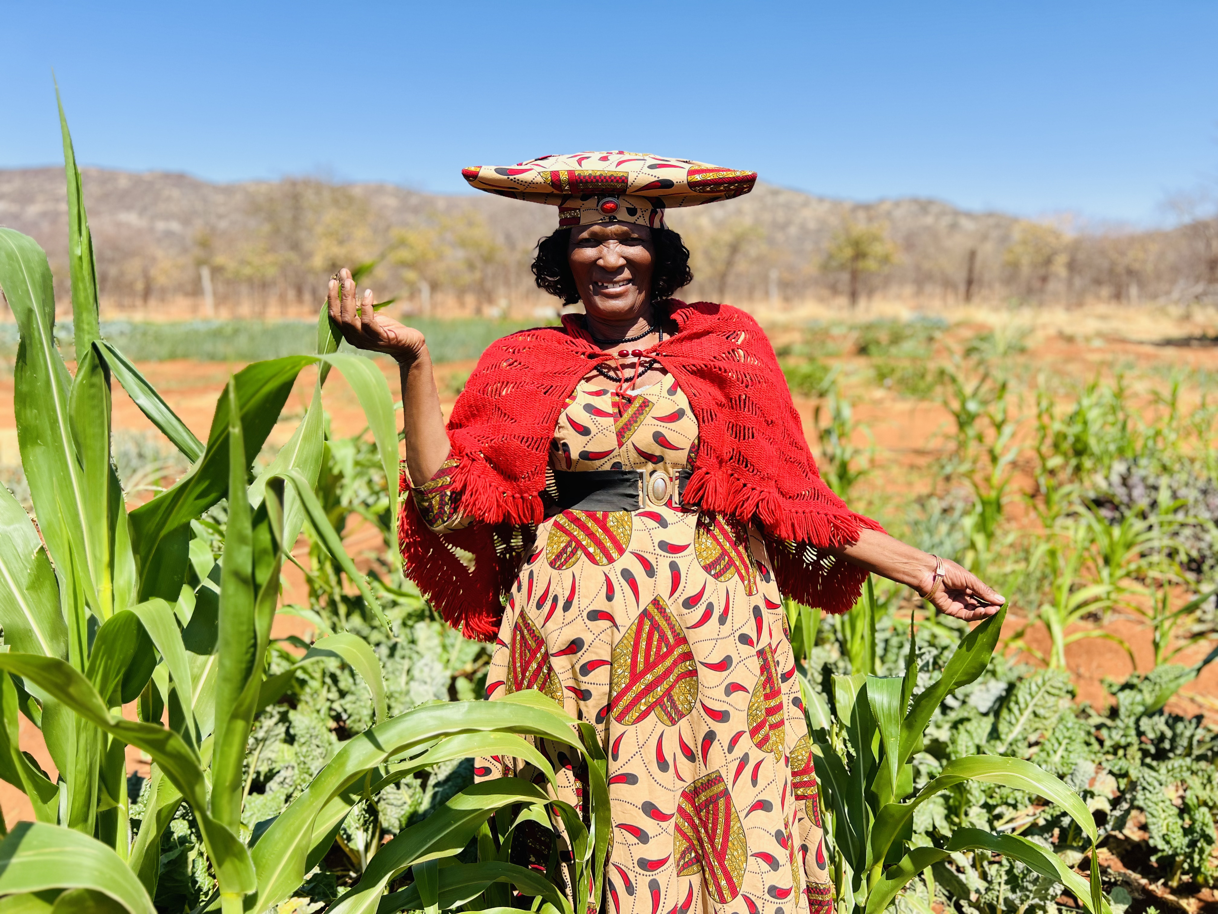 Photo: UNDP Namibia A woman stands in a field of green plants, wearing a colorful dress