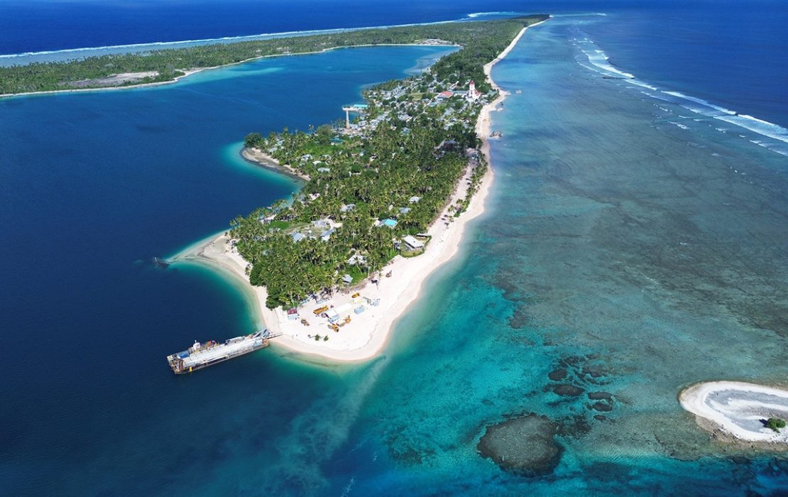 Aerial view of an atoll island in the Pacific, showing the lagoon, reefs and coastal infrastructure on a thin strip of land.