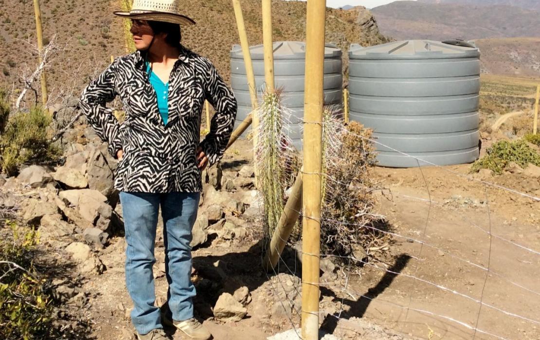 Woman standing next to water tanks in an arid field