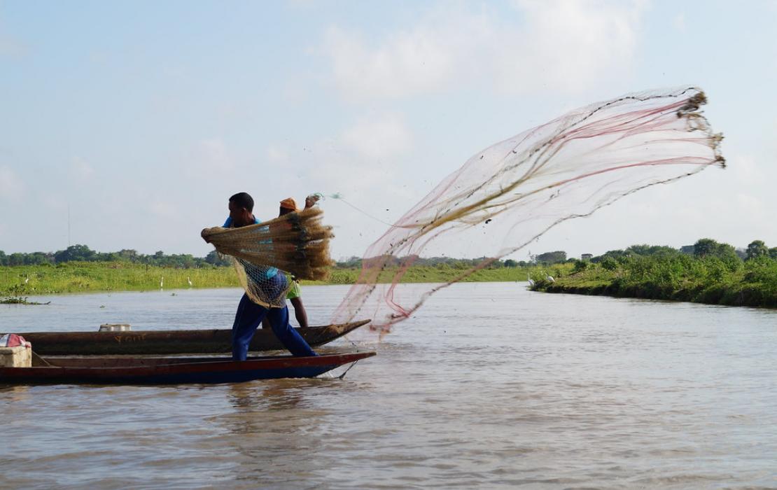 A fisherman throws a fishing net into the lake.