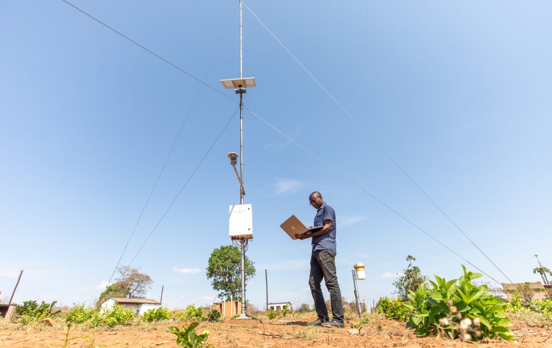 New job opportunities arising from a green economy highlight the need for updated training and skills development. Photo: UNDP Zimbabwe An engineer operates a laptop beside a tall pole equipped with solar panels and environmental sensors, part of a weather monitoring station in a field with visible vegetation under a clear, cloudless sky in Zimbabwe