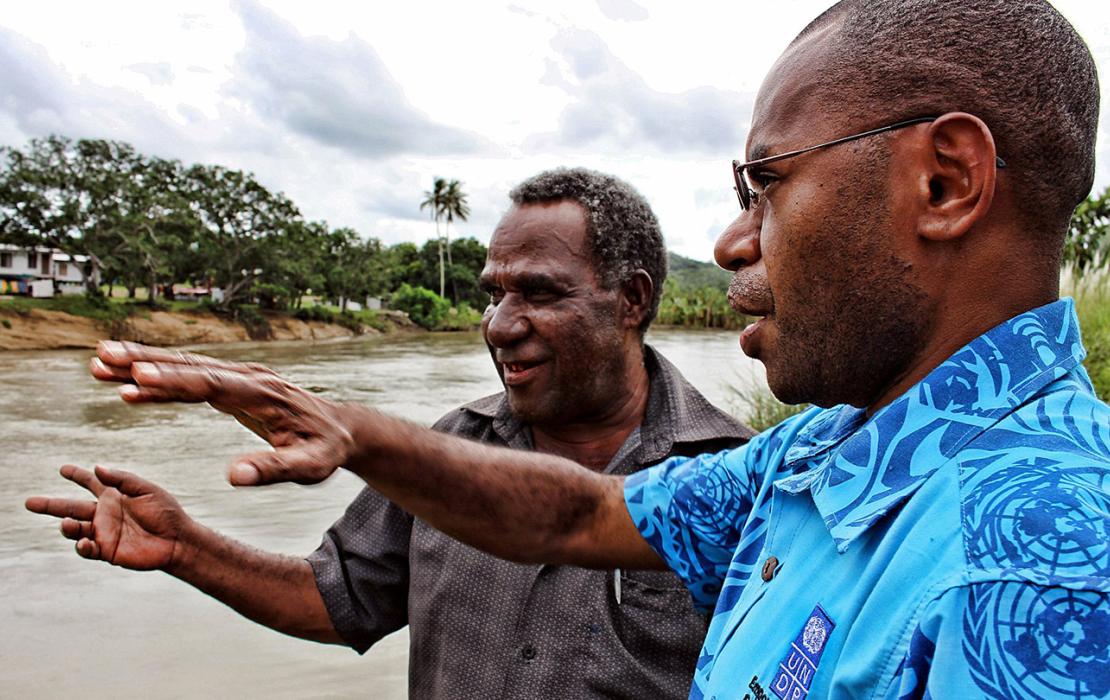 Two men gesture towards river as they discuss disaster management in Papua New Guinea.