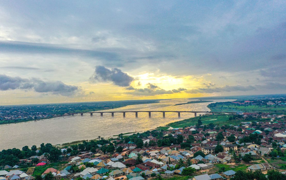 Africa’s growth shows the region's potential for economic transformation. Photo: UNDP Nigeria An aerial view of a wide river in Nigeria with a long bridge stretching across it, surrounded by a densely built town and lush green landscape under an evening sky. Photo: UNDP Nigeria