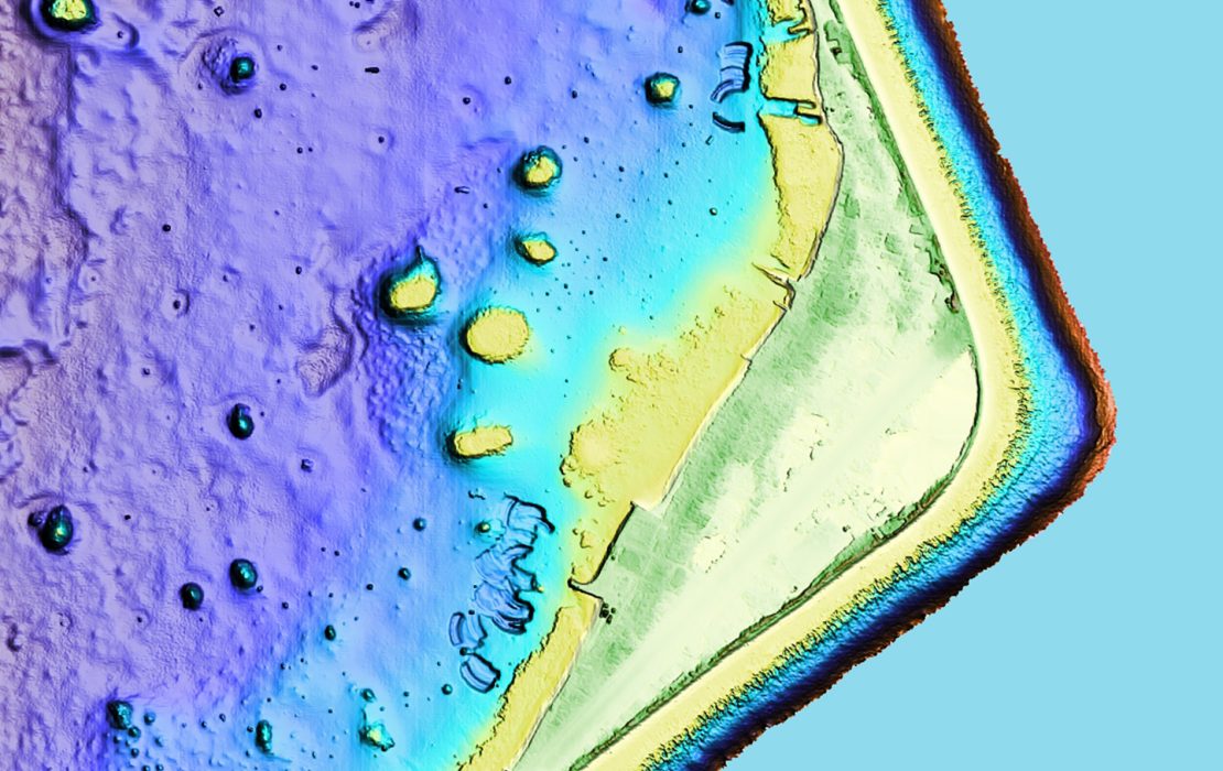 High resolution satellite image of atoll island showing in purple, blue and yellow colours the depth and shape of terrain on land and under the water.