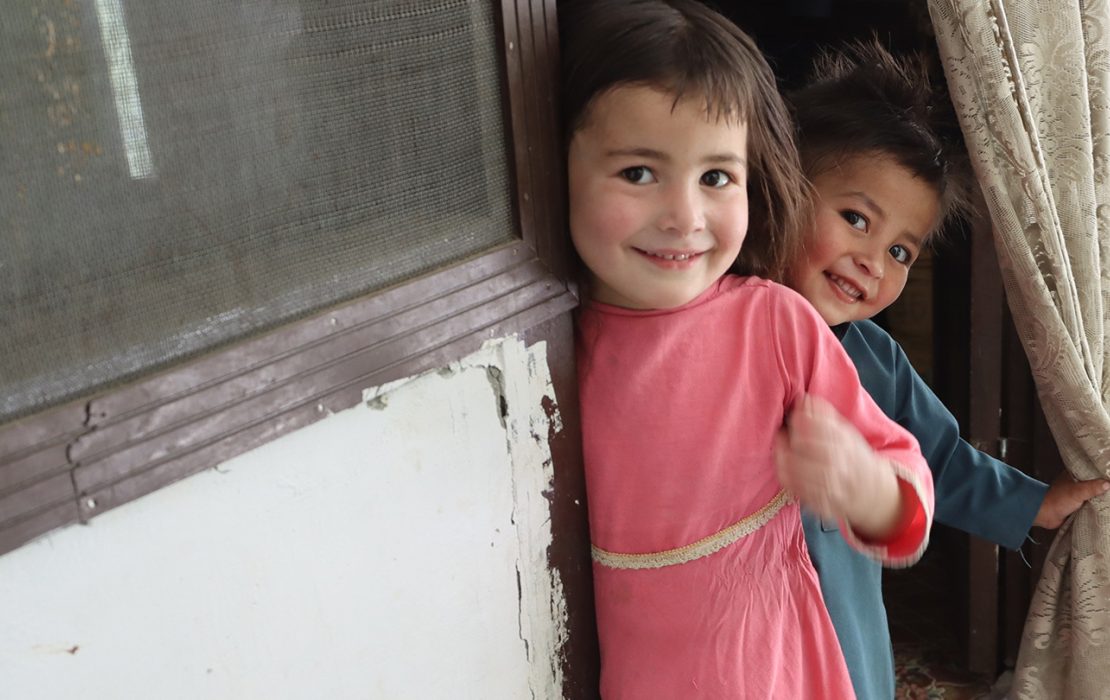 For many girls in Ghundus, water security means education security. Photo: Shameen Raza / UNDP Pakistan Two young children smile while standing in a doorway, one holding a curtain and the other leaning against the doorframe.