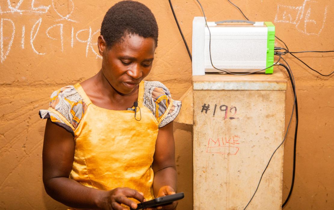 Cecelia charging her phone from the solar battery in her house. Photo: UNDP Malawi