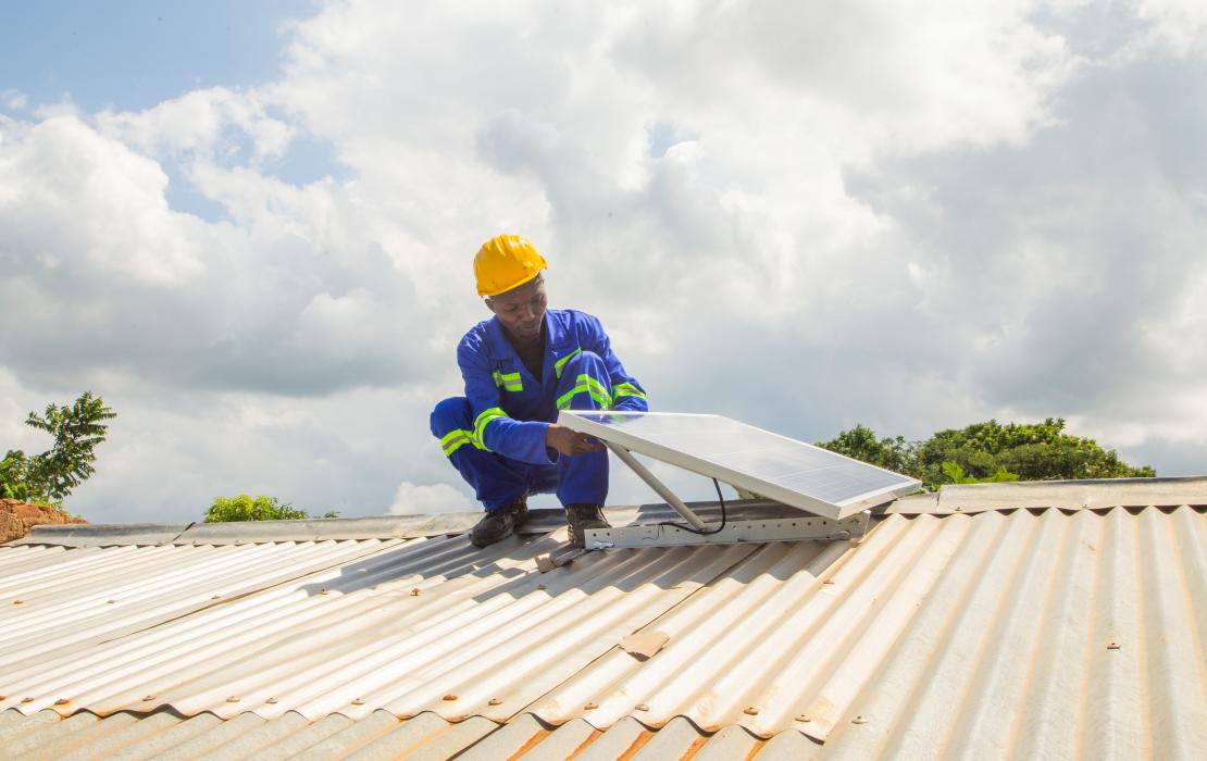 A technician installing a solar panel on a roof in Malawi