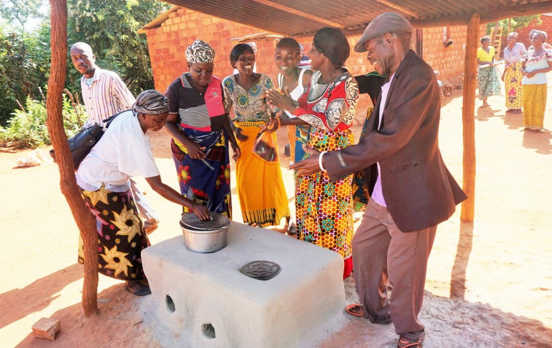 Women and men in Kenya  standing in front of a new clean cooking stove installation