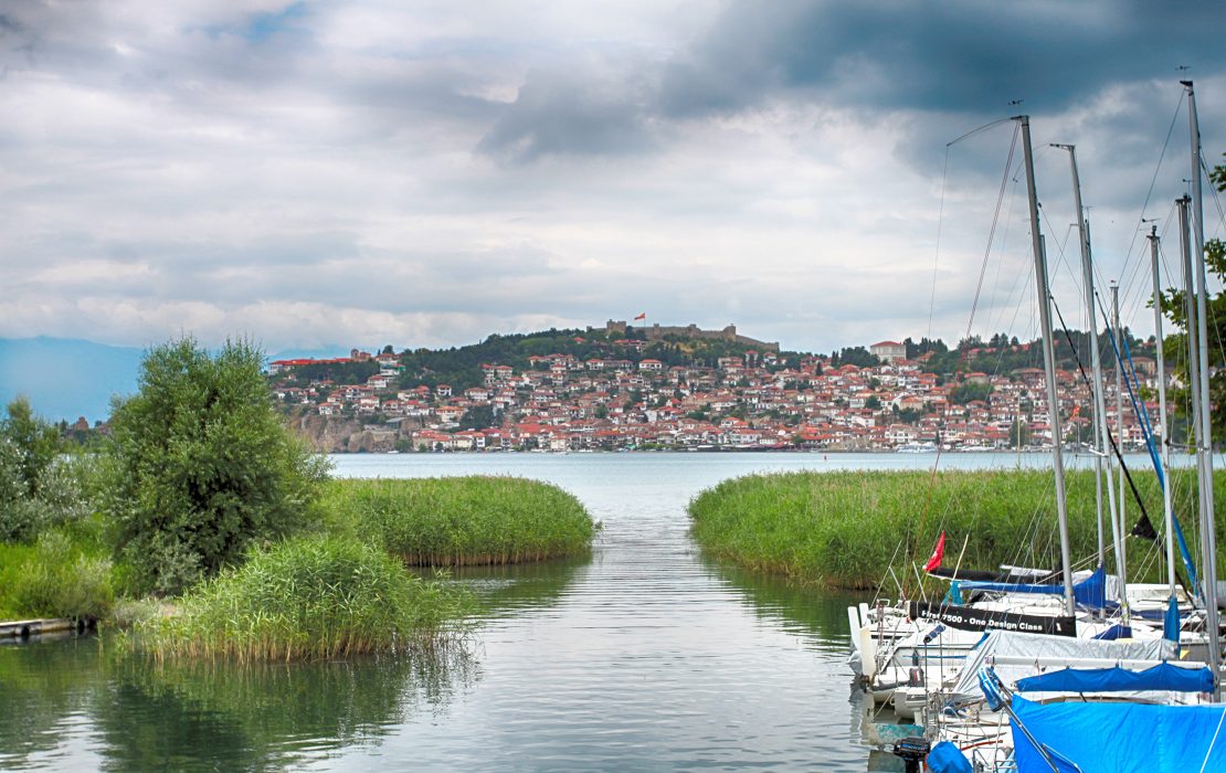 Lake Ohrid is Europe’s oldest lake, estimated to be more than two million years old. Photo: UNDP View of Lake Ohrid in North Macedonia with reed-lined water, moored sailboats in the foreground, and the town of Ohrid with its hillside houses and fortress in the background.