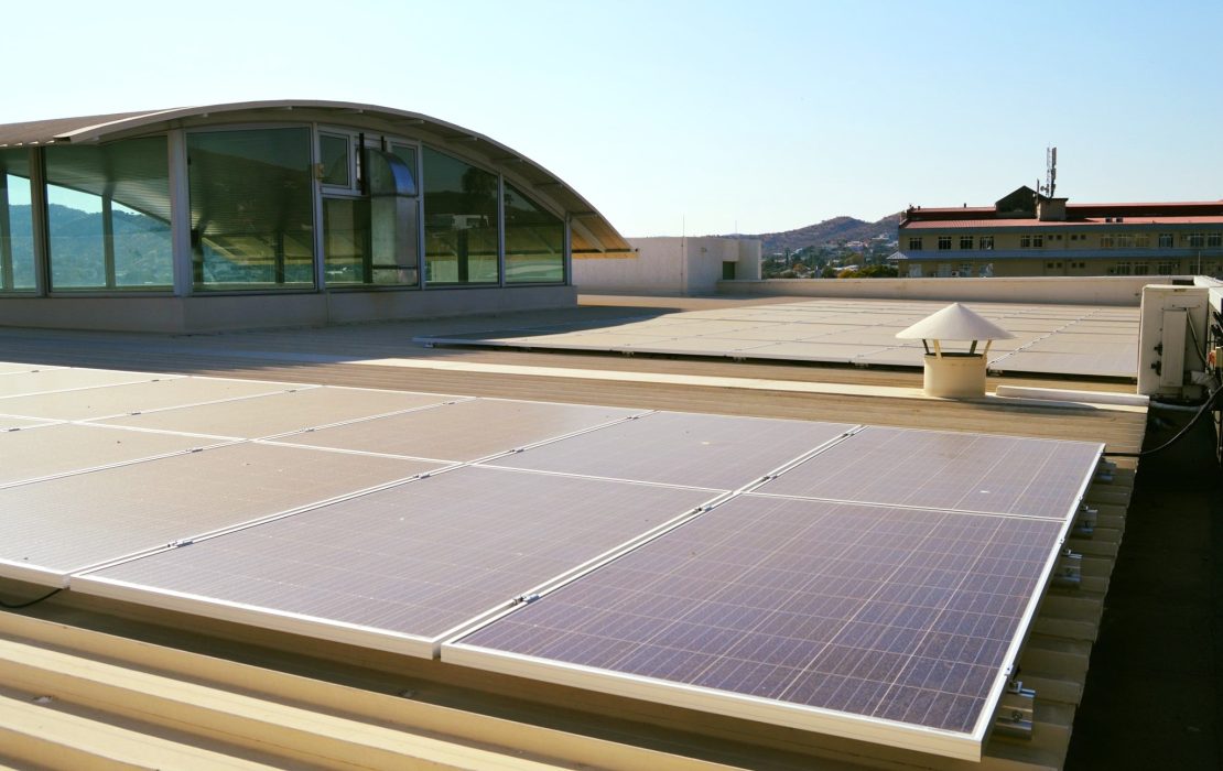Acknowledging the challenges of rapid urbanisation, Namibia's LT-LEDS focuses on resilient urban planning and climate-resilient housing to tackle climate risks. Photo: UNDP Namibia A rooftop with solar panels installed, with a curved glass-walled structure in the background and another building visible further away under a clear sky in Namibia