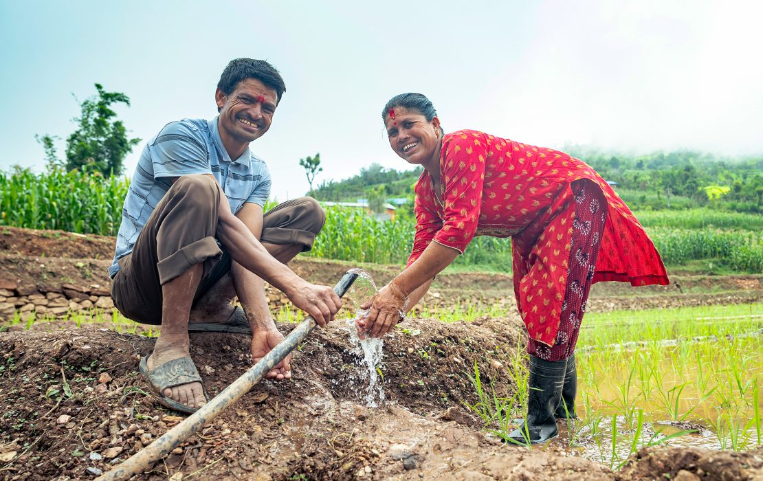 A man and woman smile as they draw water from a hose to irrigate their paddy field in eastern Nepal 