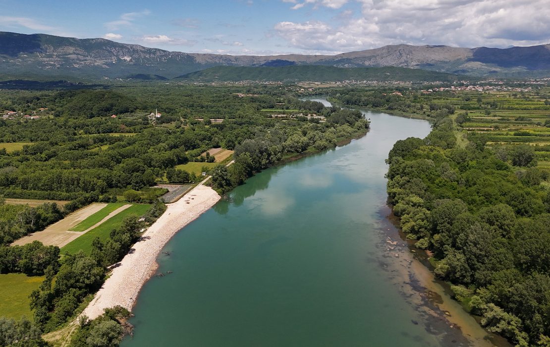 Reconstruction of the Gropat–Štodra embankment on the Bojana/Buna River, shared between Montengero and Albania and the outlet of the Drin River Basin. Photo: UNDP Montenegro Aerial view of the restored Bojana/Buna River embankment in Montenegro, with farmland and forest bordering the reinforced riverbank.