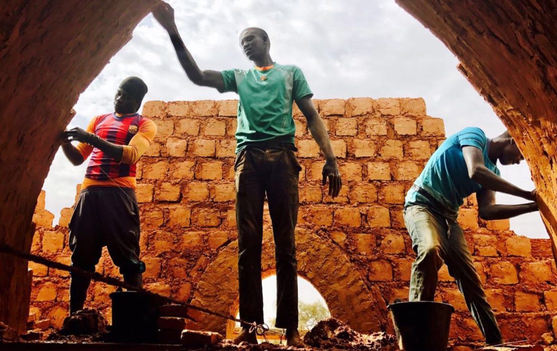 Three men constructing an arched structure using earthen bricks, reviving traditional building techniques in the Sahel to promote sustainable architecture.