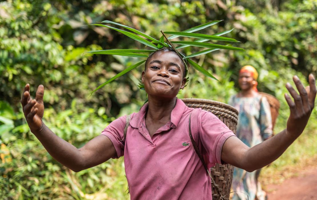 A woman wearing a hat made of tree leafs walking in a forest, Equateur region, Democratic Republic of Congo