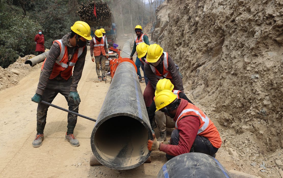 Workers in safety gear install large irrigation pipes along a rural hillside, constructing infrastructure to improve water access.