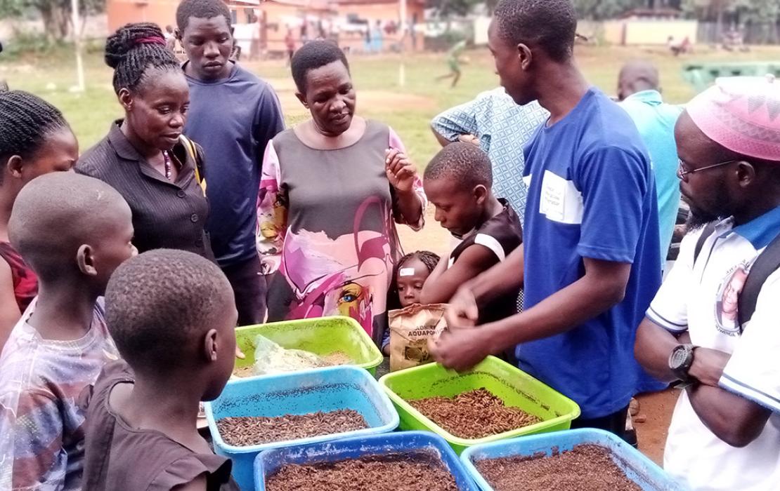 Group of people watch as man demonstrates aquaculture methods.