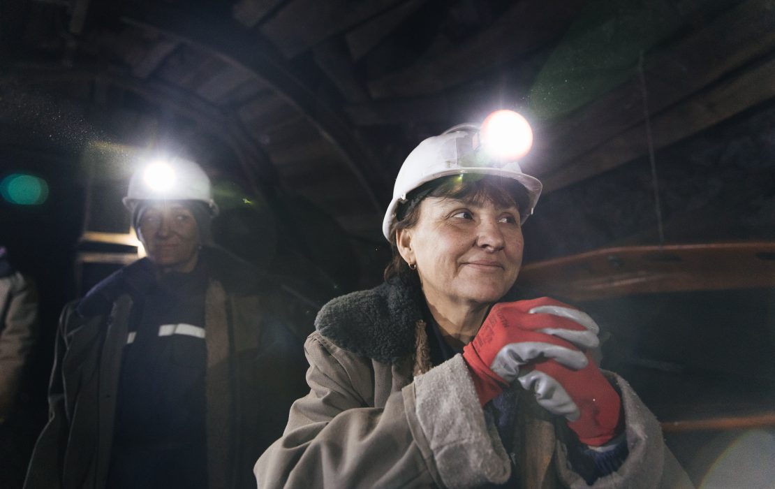 Female miners working underground in a dark coal mine tunnel wearing helmets with headlamps and protective clothing in Serbia