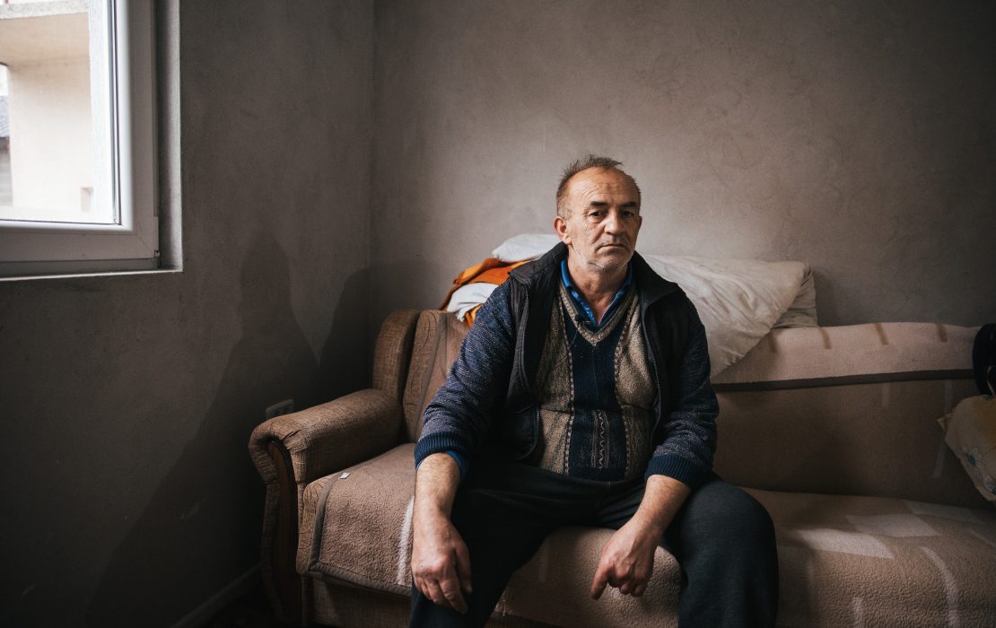 "It is an incredible feeling to finally have our own peace. Our home is warm, we use less firewood, and life is improving." says Rifat. Photo: UNDP Serbia Elderly man sitting alone on a couch in a modest home, looking serious, representing rural life and everyday struggles in Serbia.