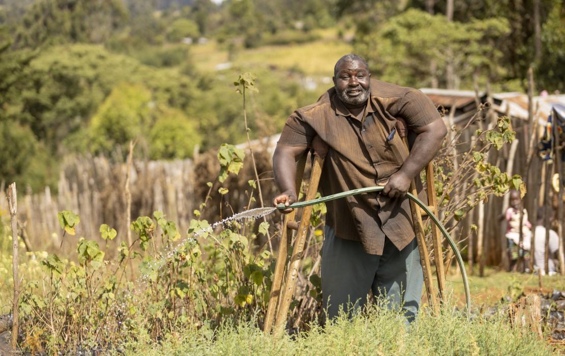 Un homme porteur de handicap qui arrose des plants d'arbres