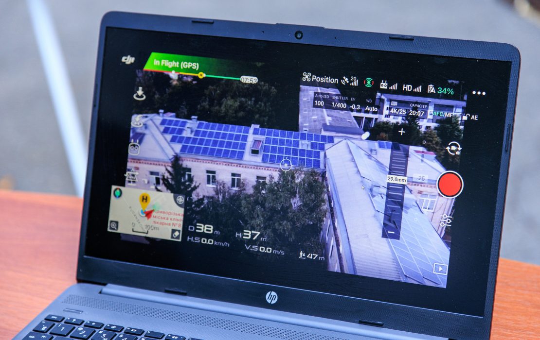 A laptop screen displays drone footage showing solar panels installed on the roof of a hospital building in Kryvyi Rih, Ukraine.