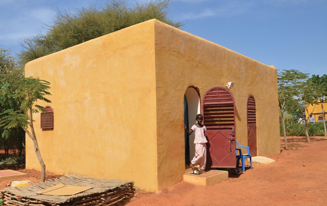 Un niño está de pie en la puerta de una casa con bóveda nubia en el Sahel