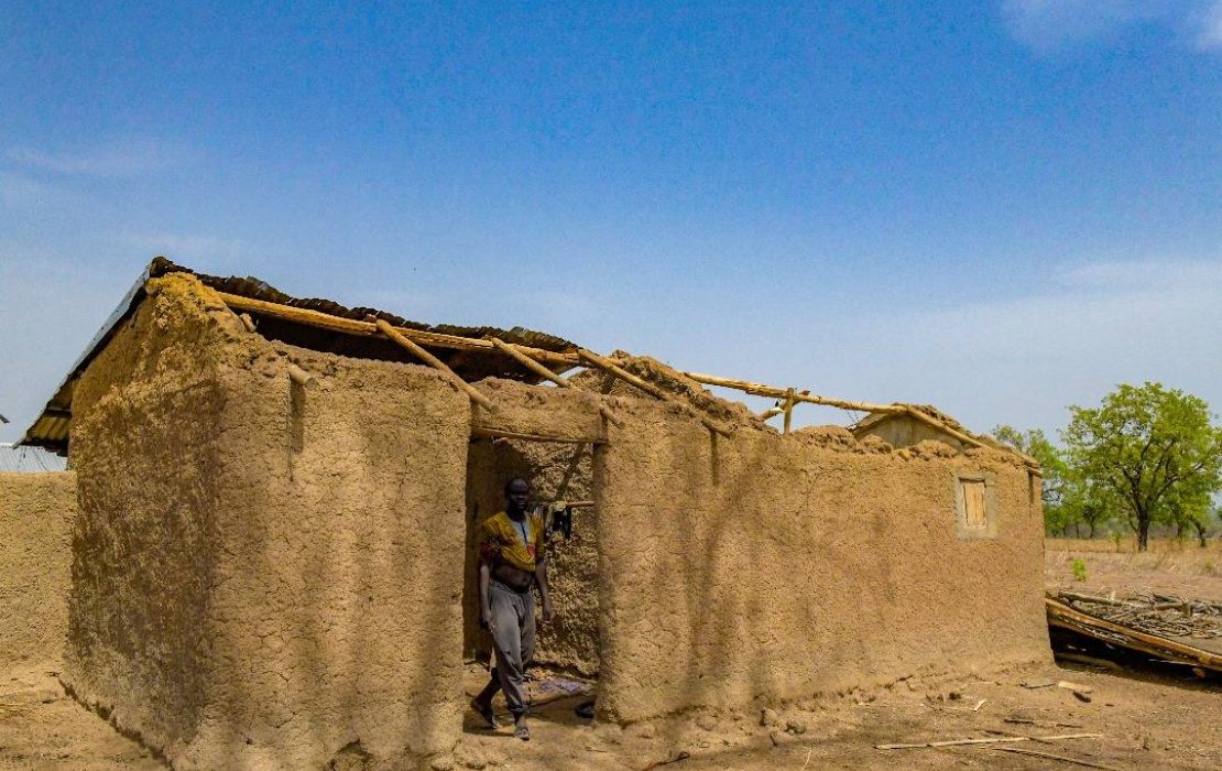 Climate shocks in Togo are regularly affecting the livelihoods of vulnerable populations in rural areas. Photo: UNDP Togo A man stands in the doorway of a partially collapsed mud-brick house with a thatched roof, set in a rural landscape with dry, barren ground and minimal vegetation in Togo