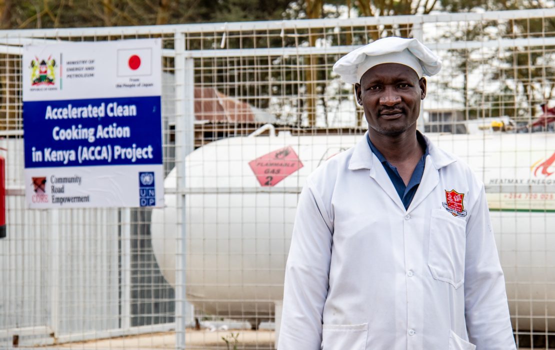 A man standing in Kenya near a panel on the UNDP clean cooking project