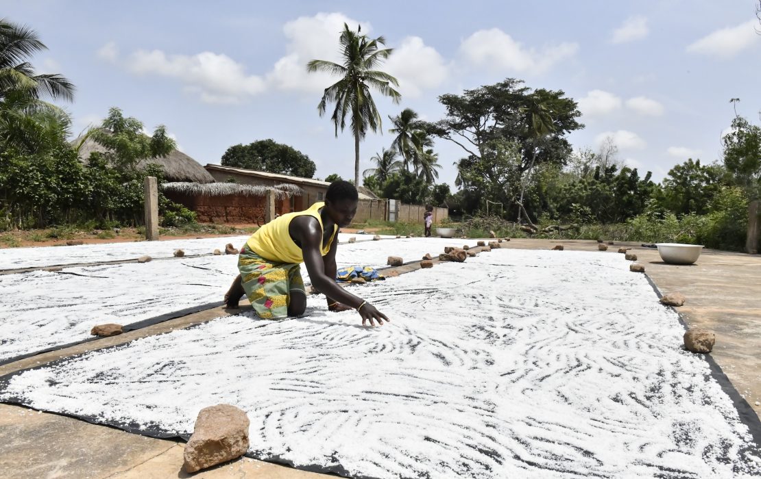 Togo's LT-LEDS helps turn targets into action at local levels, supporting communities that rely on agriculture for their livelihoods. Photo: UNDP Togo A man spreads cassava on large black mats to dry under the sun, with palm trees, greenery, and buildings in the background under a partly cloudy sky in Togo