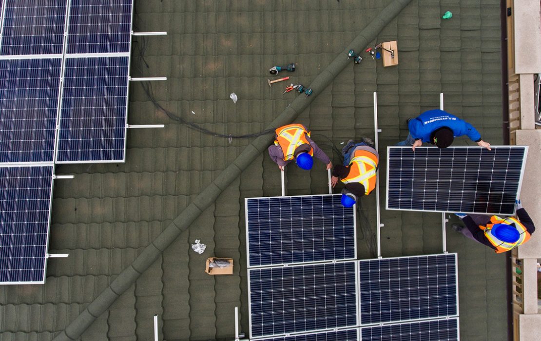 Workers install solar panels on roof