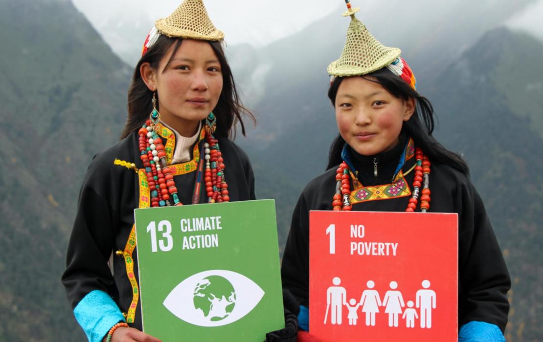Two women in Bhutan hold up signs of SDG13 (Climate Action) and SDG1 (No Poverty).