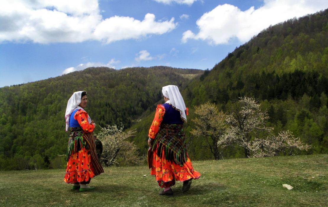 Women in Tajikistan dressed in traditional clothing look at scenic mountains.