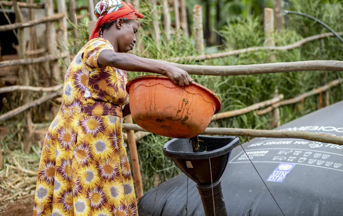 A woman pouring organic waste to be used for cooking, hot water, and small electrical generators.