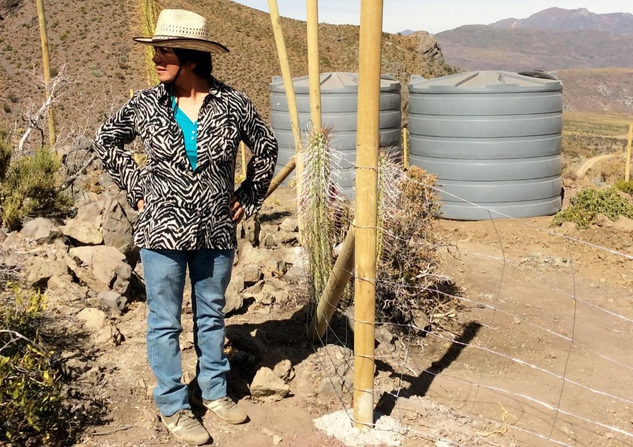 Woman standing next to water tanks in an arid field