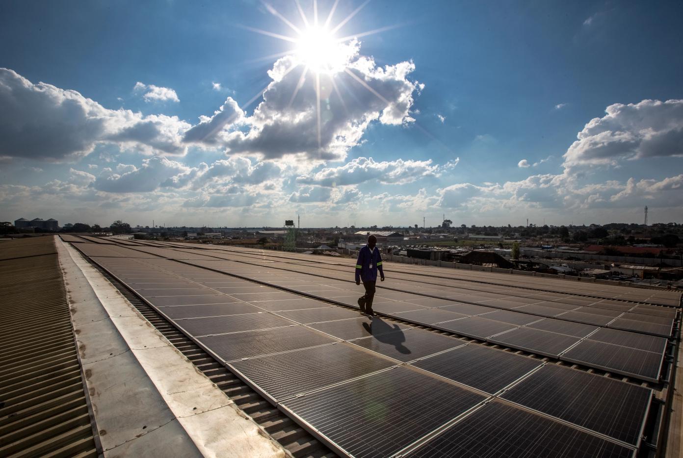 Un technicien marchant au milieu de panneaux solaires installés sur un toit à Lusaka, en Zambie