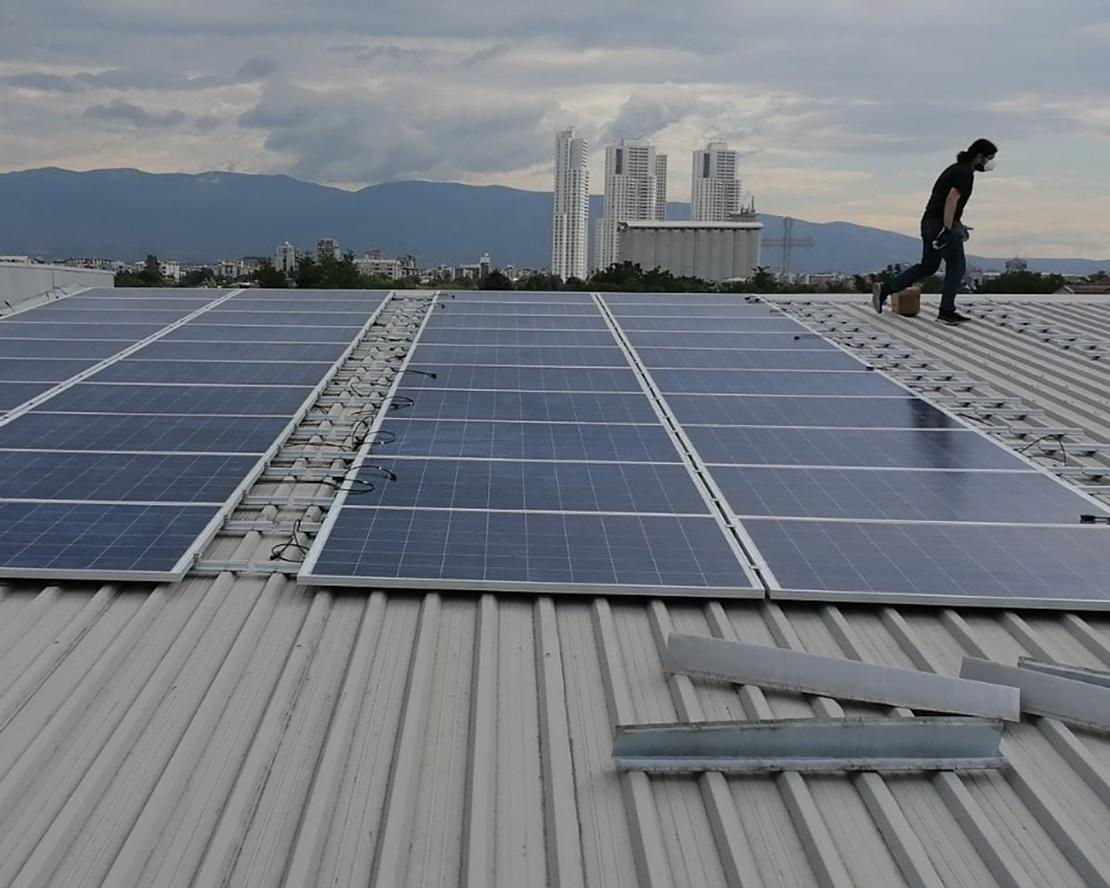 Solar panels with a city and mountain scape in the background, cloudy, daytime.