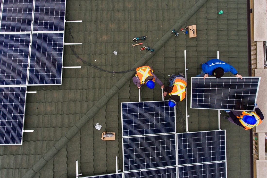 Workers install solar panels on roof