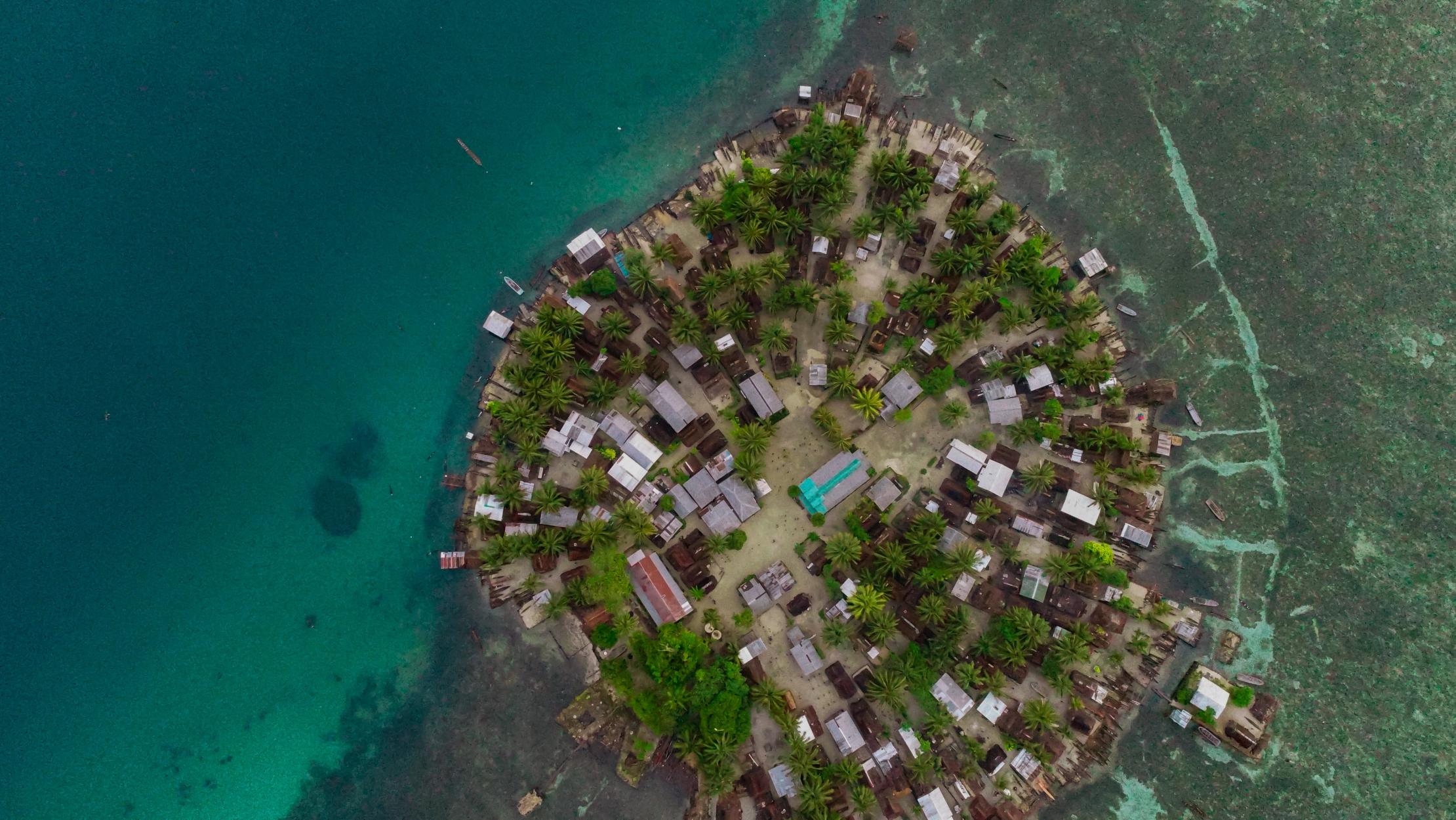 Aerial view of populated circular island with houses, surrounded by blue ocean.