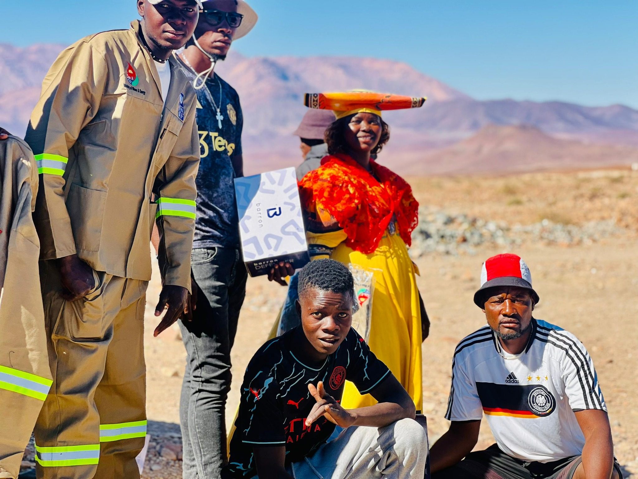 Un groupe de personnes en Namibie, debout en plein air avec des montagnes en arrière-plan sous un ciel bleu