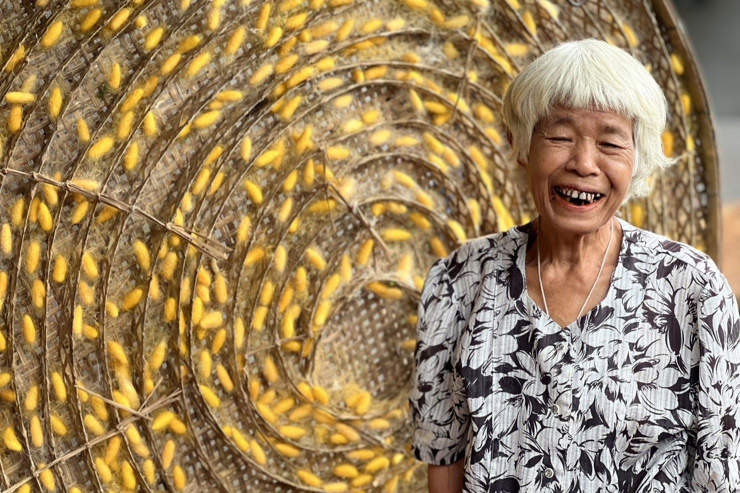 Soom Yeunyong, a community member from Surin Province, posing in front of the silk cocoons. Photo: Foundation for Community Soul Soom Yeunyong with the silk cocoons