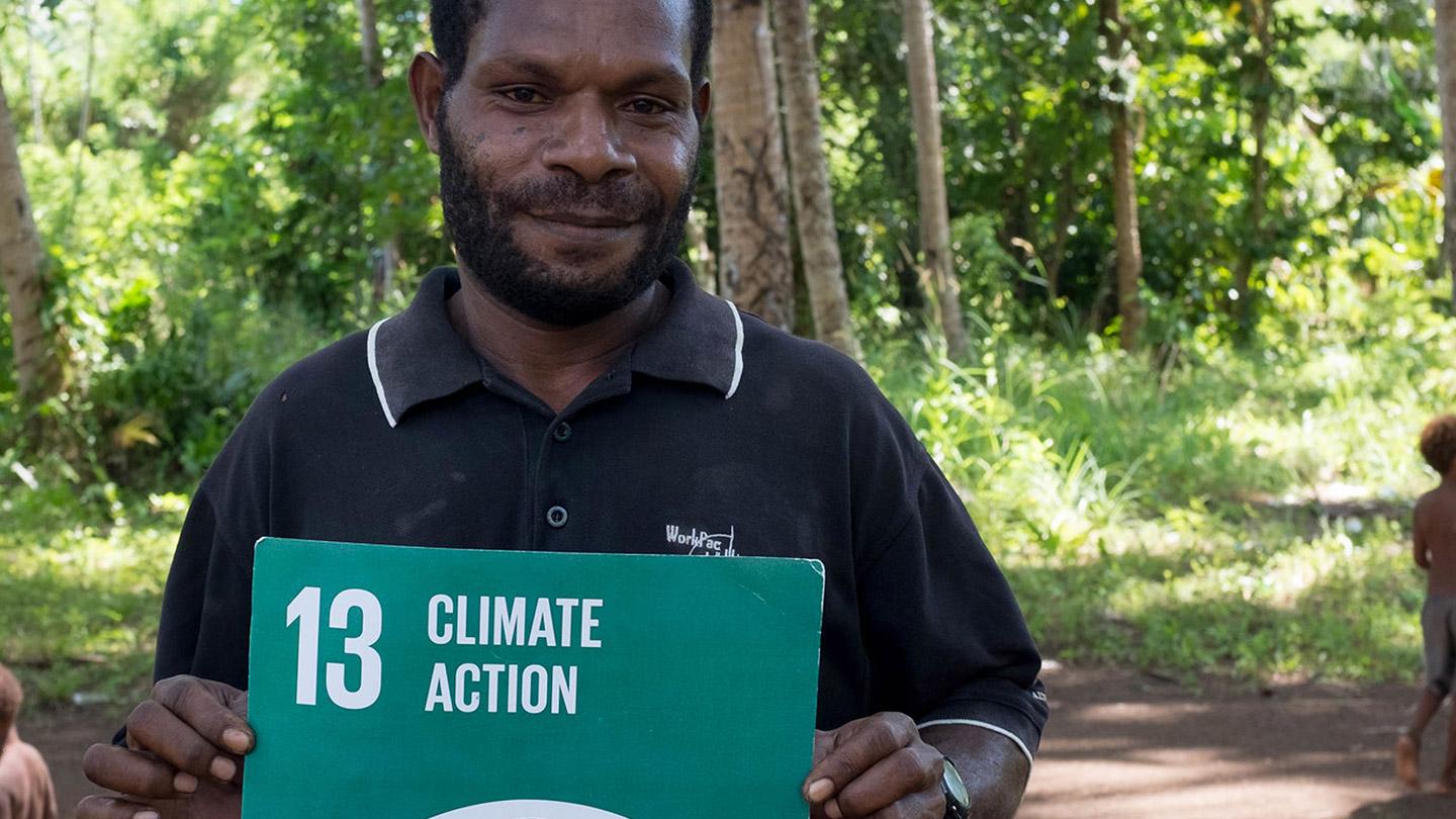 Man from Papua New Guinea poses for photo holding sign for Sustainable Development Goal 13, "Climate Action".