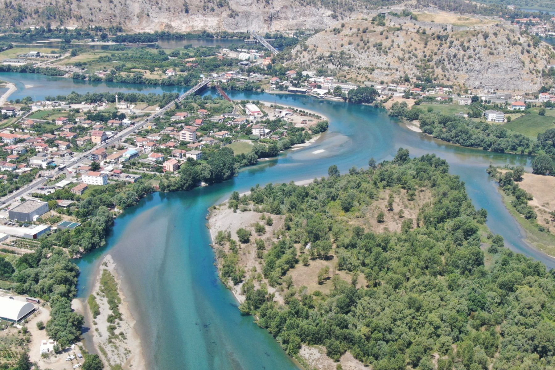 The Drin River Basin is one of the most flood-prone regions in the Western Balkans. Photo: Sead Sadiku, Director at the Administration Office of Drin-Buna Water Basin Aerial view of the Drin River Basin with winding turquoise waterways, green forests, and nearby towns in Albania.