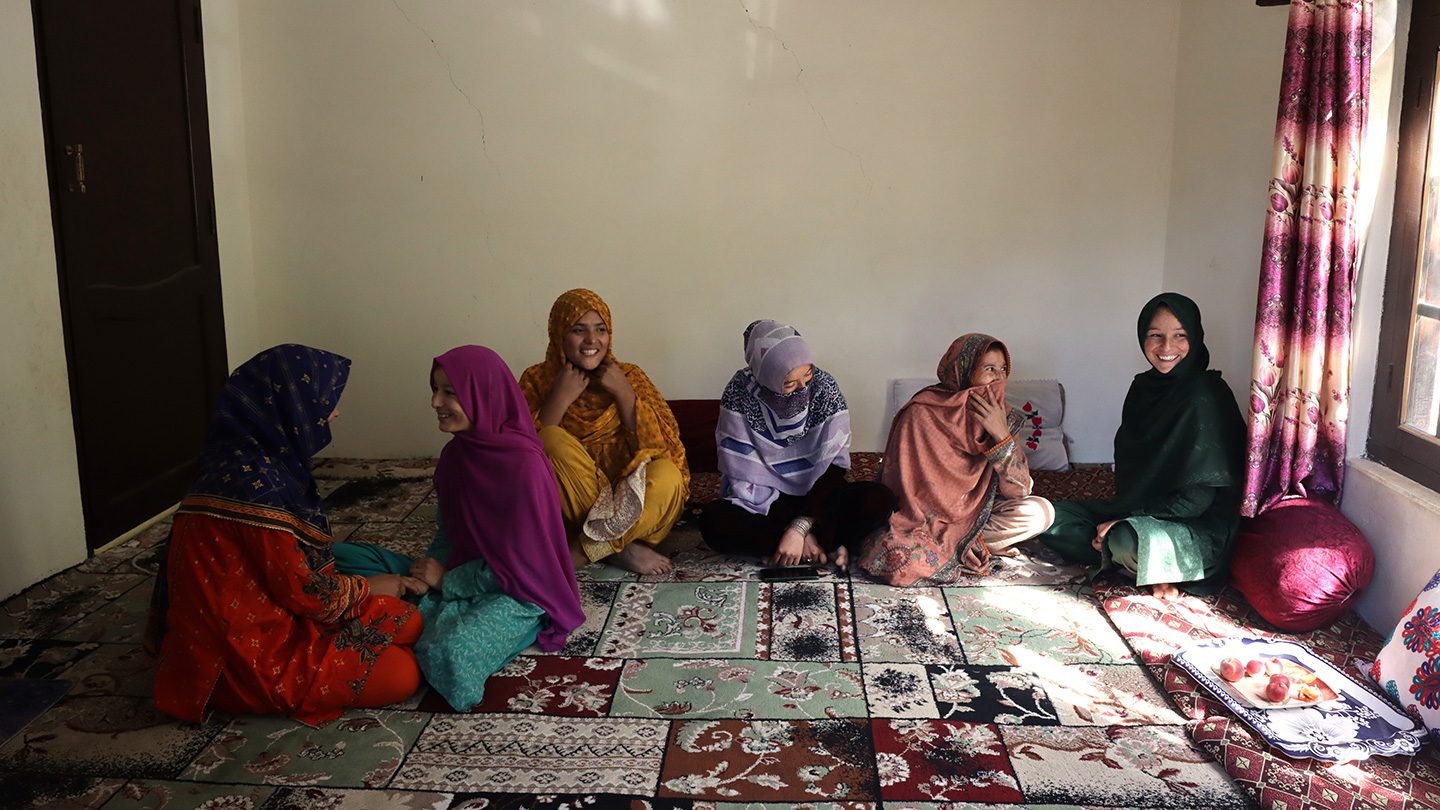 For the people of Ghundus, access to water is more than just an agricultural necessity – it is the foundation of economic stability, gender equality and educational opportunity. Photo: Shameen Raza / UNDP Pakistan Seven women and girls sit together on a patterned carpet inside a sunlit room, smiling and talking near a window.