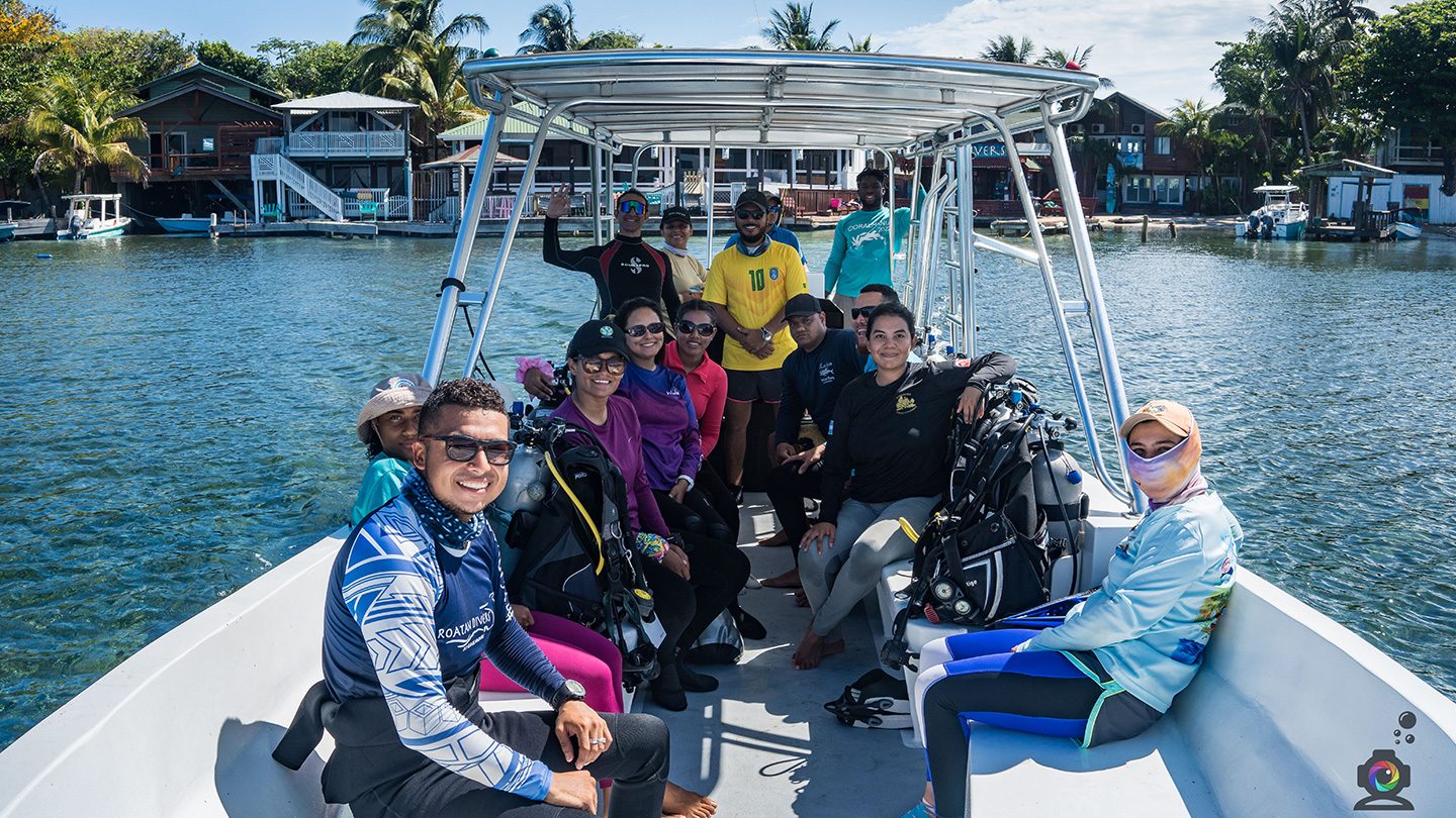 A group of scuba divers and conservation volunteers sit together on a boat, preparing for reef restoration work in Honduras.