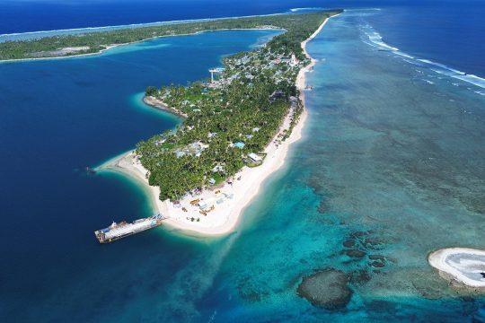 Aerial view of an atoll island in the Pacific, showing the lagoon, reefs and coastal infrastructure on a thin strip of land.