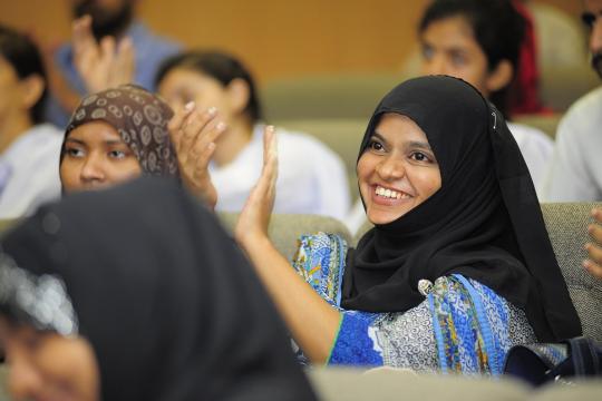 Young person in Pakistan smiling and applauding at an event