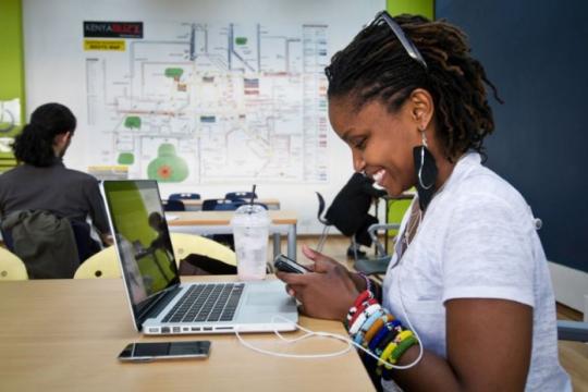 Une jeune femme utilisant son téléphone assise devant son ordinateur