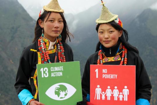 Two women in Bhutan hold up signs of SDG13 (Climate Action) and SDG1 (No Poverty).